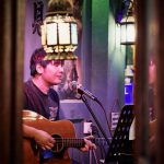 Músico canta e toca violão em uma apresentação musical em ambiente interno.