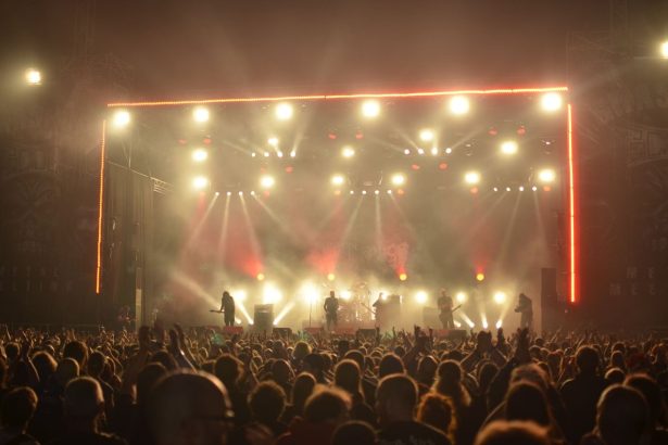 Banda se apresenta em um palco iluminado diante de uma plateia durante um show de rock.