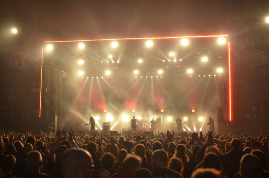 Banda se apresenta em um palco iluminado diante de uma plateia durante um show de rock.