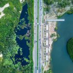 Vista aérea de trecho litorâneo com faixa de areia, via, áreas urbanizadas e vegetação.