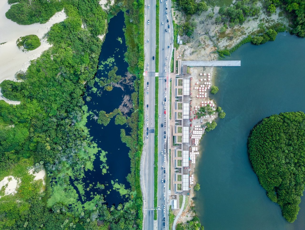 Vista aérea de trecho litorâneo com faixa de areia, via, áreas urbanizadas e vegetação.