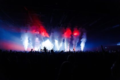 Público acompanha um show ao vivo diante de um palco iluminado por fumaça e luzes coloridas.