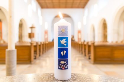 Fonte batismal com vela acesa no interior de uma igreja, em referência a uma cerimônia cristã de batismo