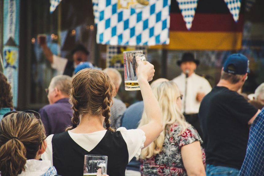 Público reunido em uma Oktoberfest ao ar livre, com canecas de cerveja levantadas em clima de celebração.